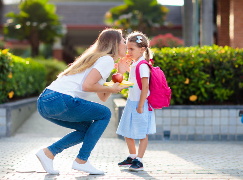 Mama całująca córkę przed szkołą z różowym plecakiem